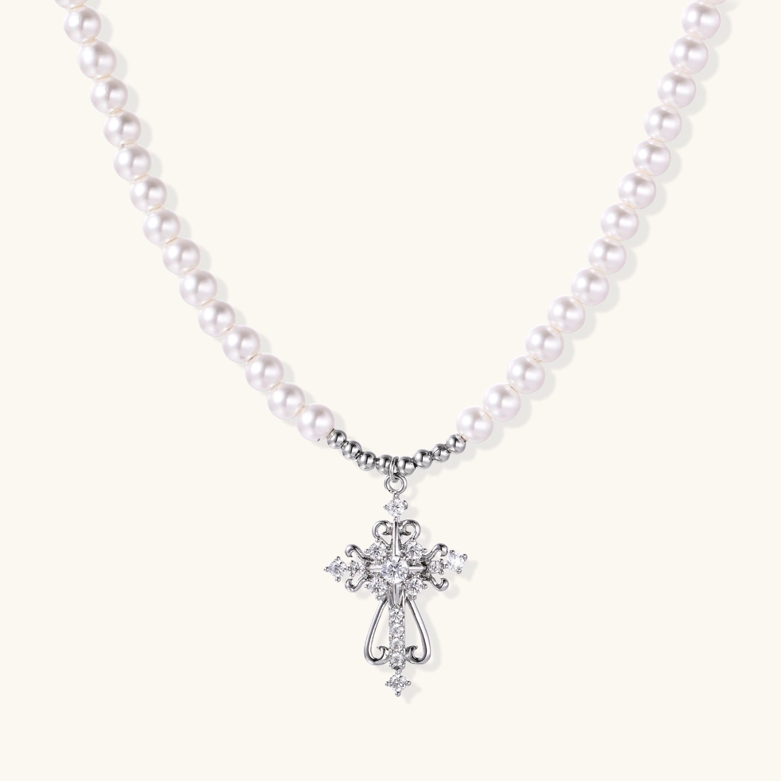 White pearl necklace with ornate silver cross pendant featuring zirconia crystals on cream background.
